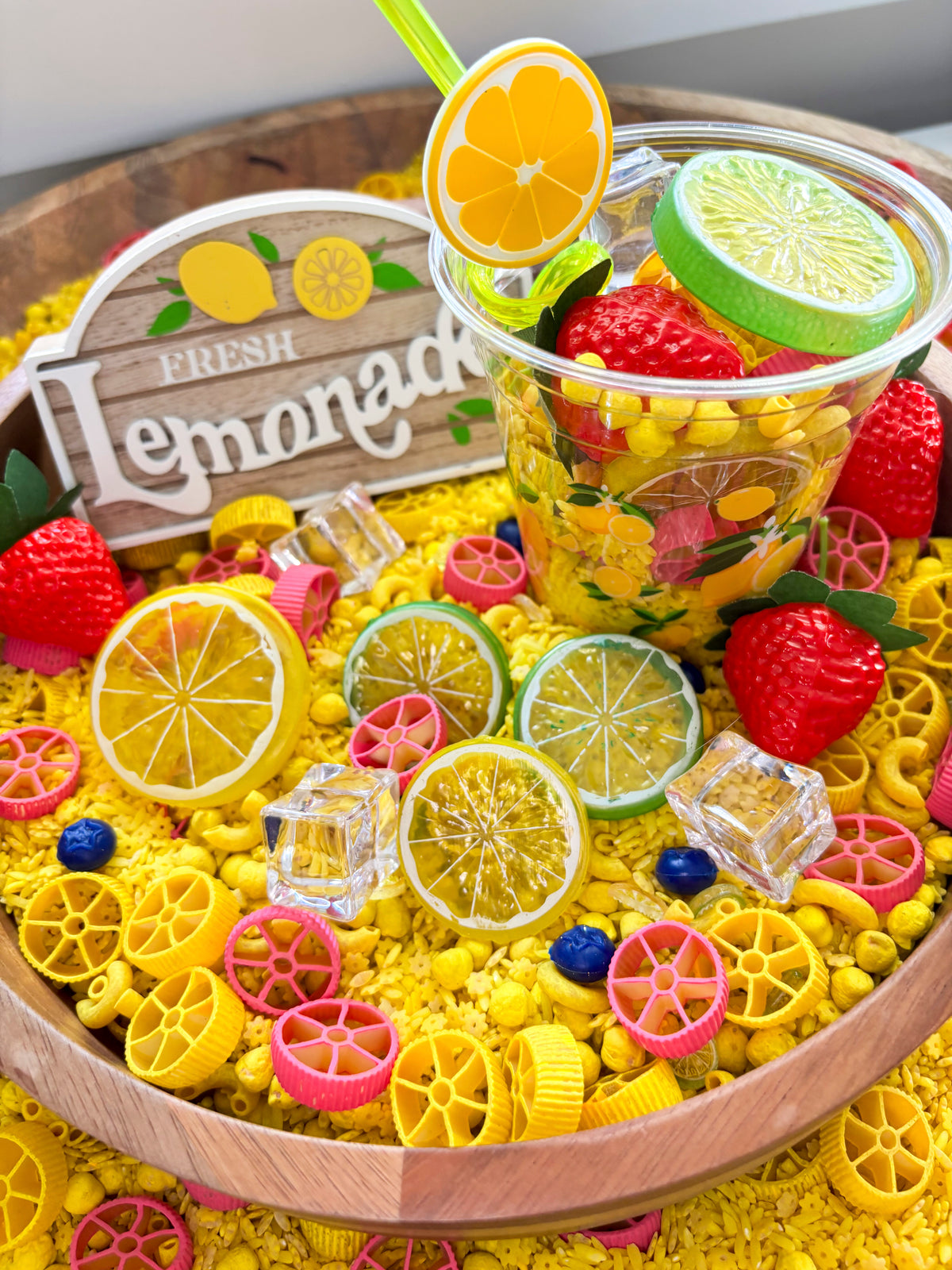 Lemonade sensory kit with colorful sensory filler, citrus slices, strawberries, and a lemonade cup for preschool sensory play.