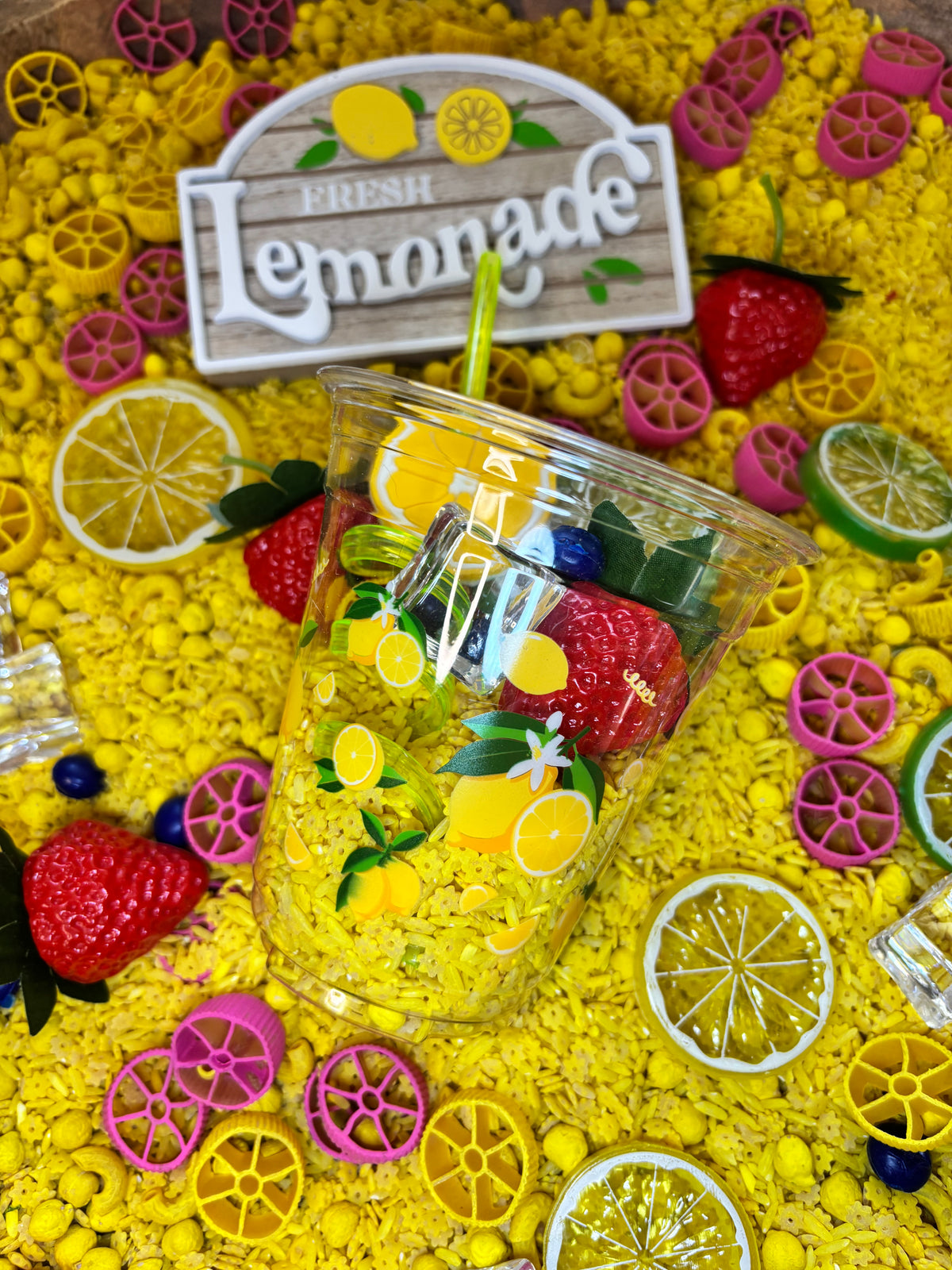 Overhead view of a lemonade sensory kit with citrus slices, colorful filler, and a lemonade cup for imaginative play.