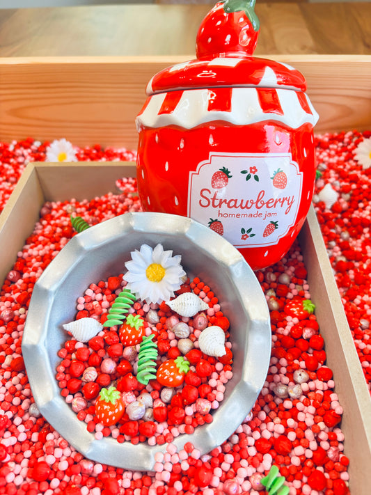 Strawberry sensory kit with colorful sensory filler and strawberry-themed manipulatives for preschool learning.